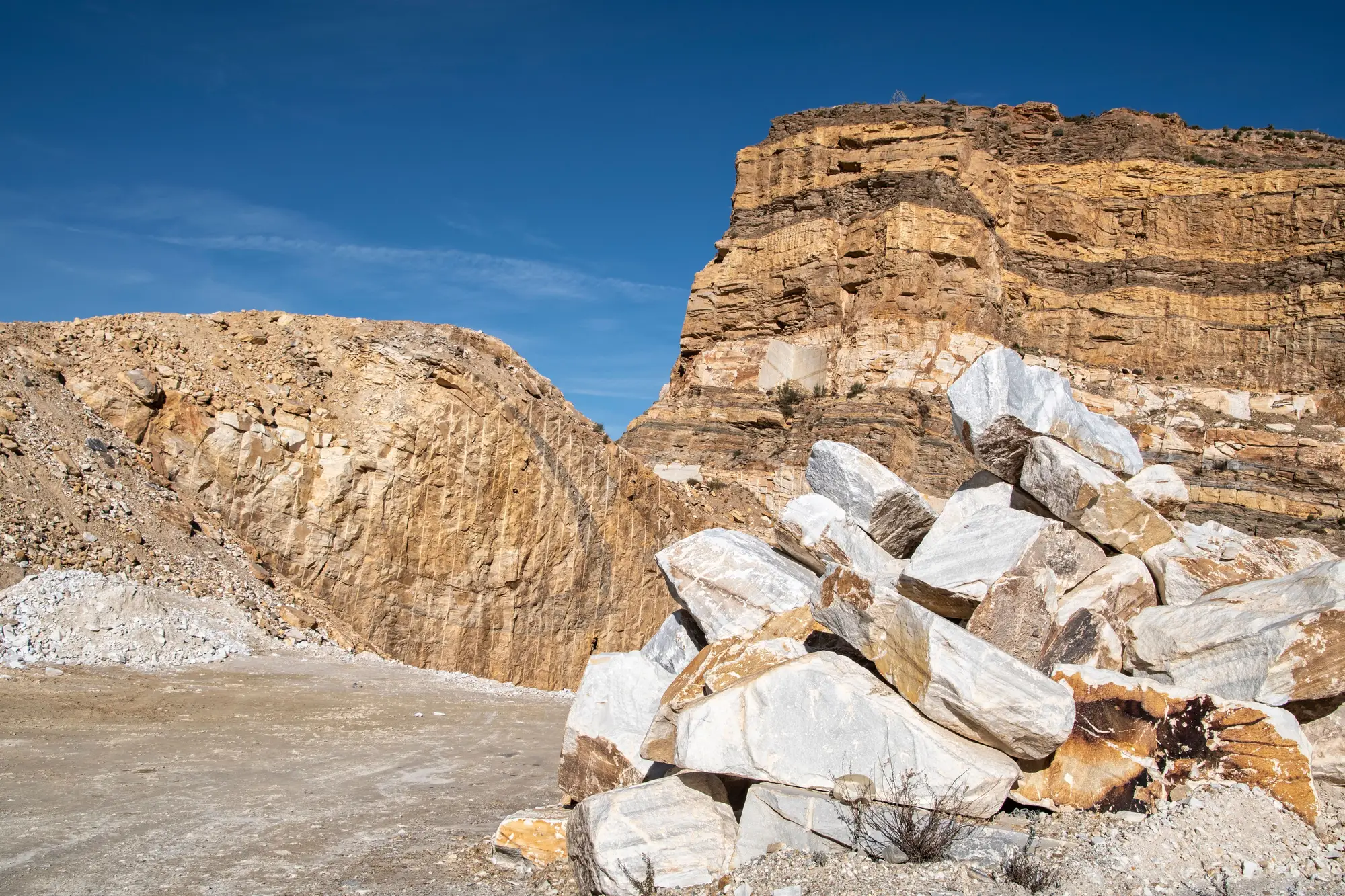 Broken stone stacked below a layered quarry face under a clear sky
